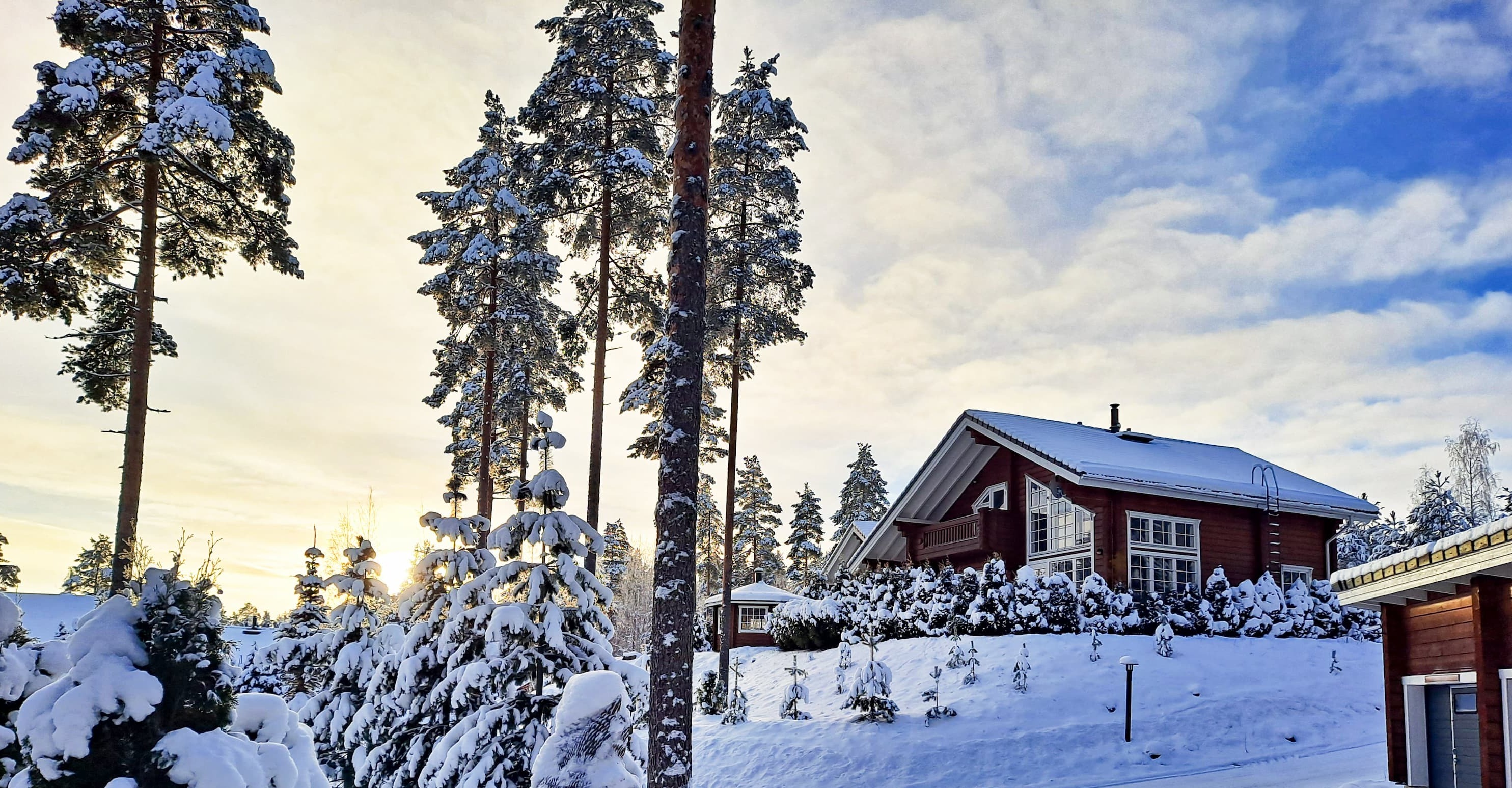 Winter cottage at the Tahko ski resort in Finland: a wooden cottage surrounded by snow-covered trees against a backdrop of blue sky and a winter sunset