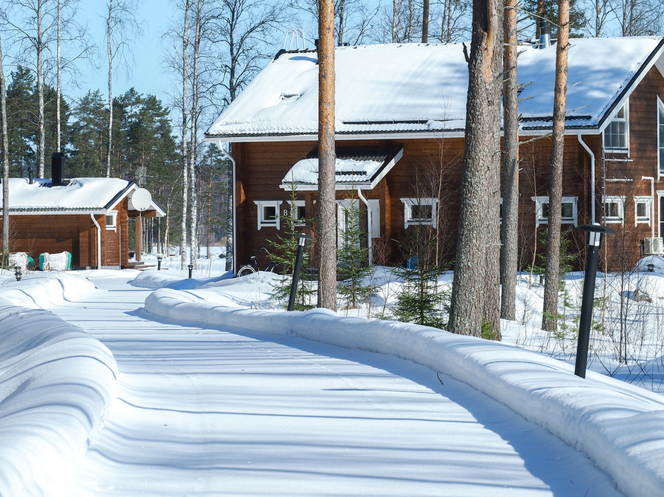 Snowy road to a cottage on the shores of Lake Saimaa, Finland: wooden cottage with a lakeside sauna surrounded by a winter forest on a sunny day